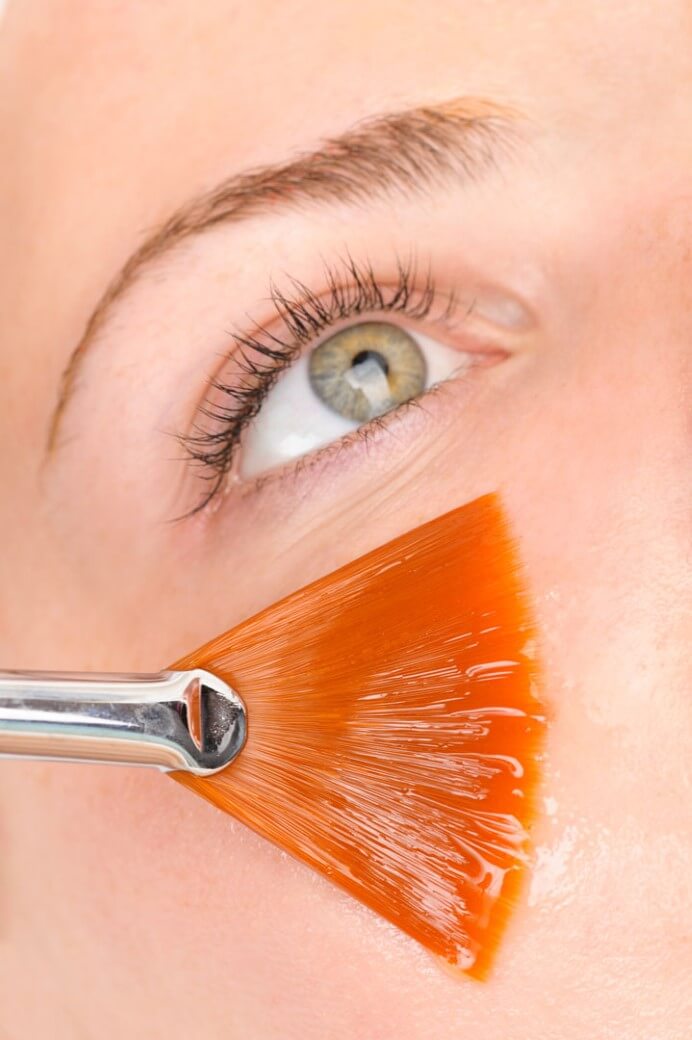 A brush delicately applying a facial solution to a person's cheek.